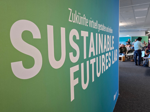Large green wall with the words “SUSTAINABLE FUTURES LAB” and German subtitle, at an event.